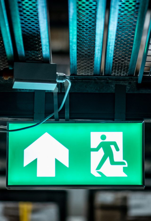 Green emergency exit sign or fire exit sign showing the way to escape with arrow symbol.